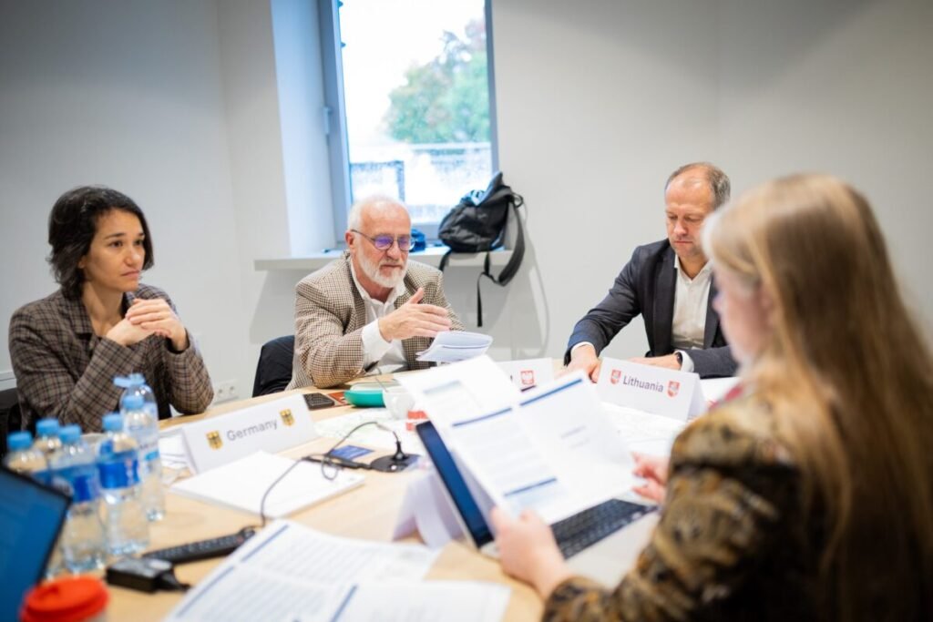 Participants around a table at ISM University in Vilnius, behind name cards for Germany, Poland and Lithuania. One gestures as he speaks.